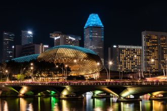 Vista noturna da baía de Marina Bay, em Singapura, com a Esplanada e edifícios iluminados ao fundo.