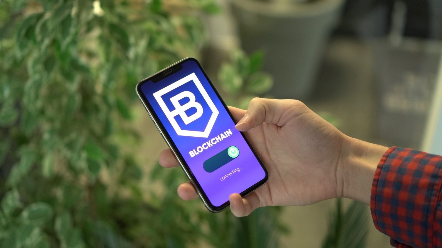Mão segurando um smartphone com um aplicativo de blockchain exibido na tela