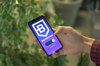 Mão segurando um smartphone com um aplicativo de blockchain exibido na tela