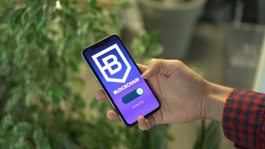 Mão segurando um smartphone com um aplicativo de blockchain exibido na tela