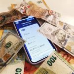 Smartphone com conversor de moedas cercado por notas de dólar e euro, destacando taxas de câmbio.