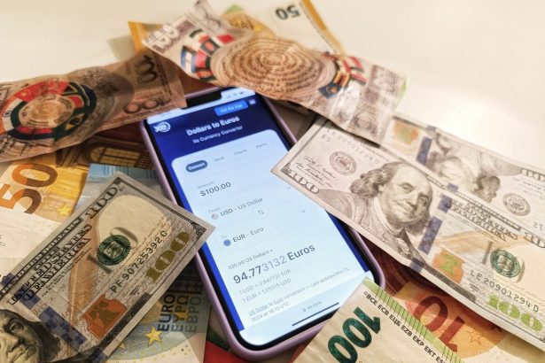Smartphone com conversor de moedas cercado por notas de dólar e euro, destacando taxas de câmbio.