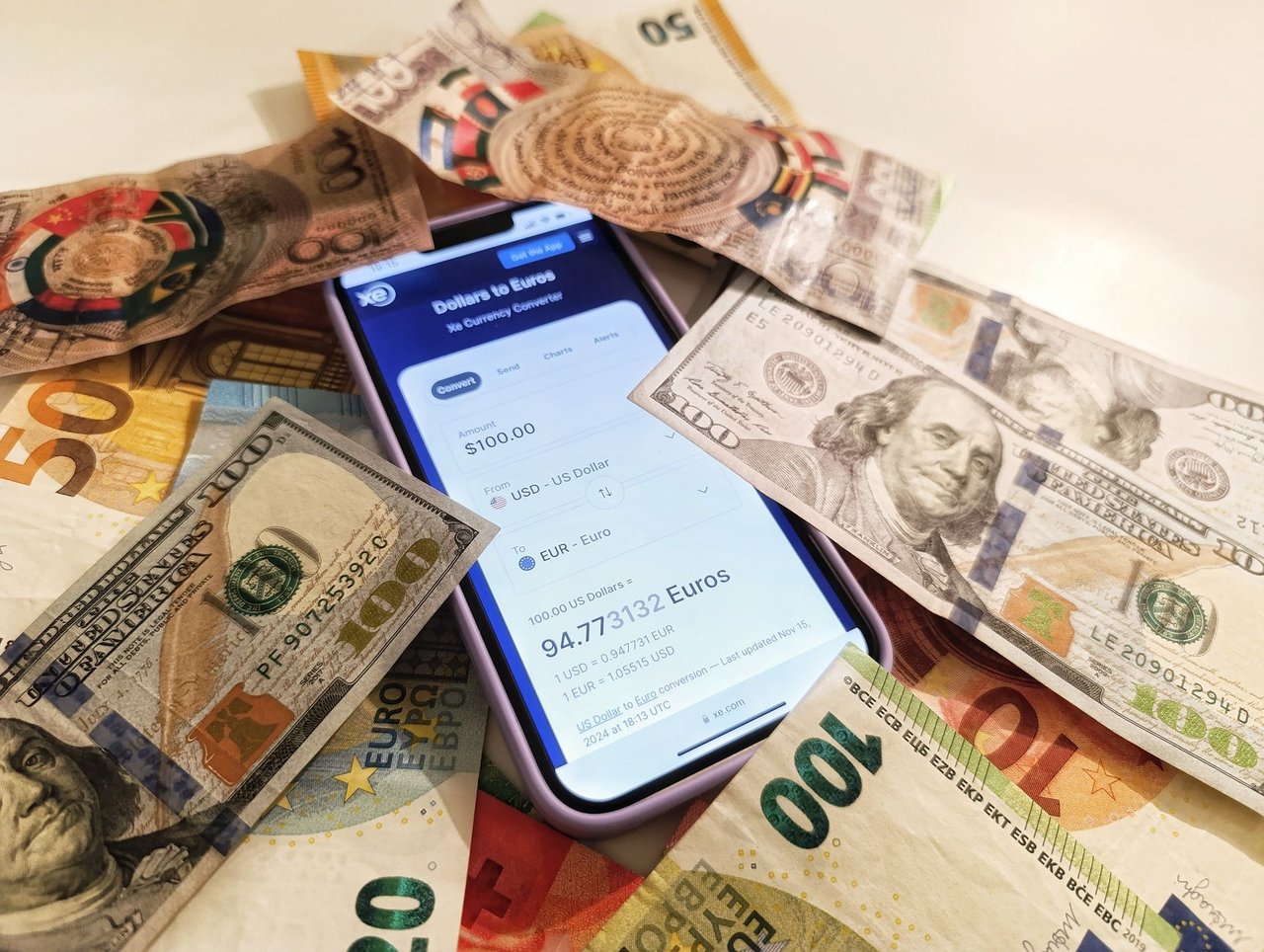 Smartphone com conversor de moedas cercado por notas de dólar e euro, destacando taxas de câmbio.